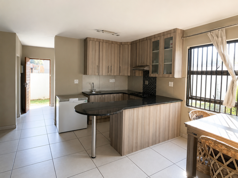 Modern kitchen featuring laminate cabinetry, granite countertops with a breakfast bar, and ceramic floor tiles, leading to an exterior doorway.