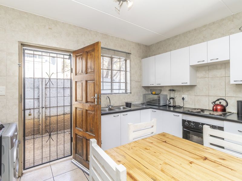Functional kitchen featuring white cabinetry, built-in oven and hob, tiled splashbacks, and direct access to an exterior courtyard through a security gate.