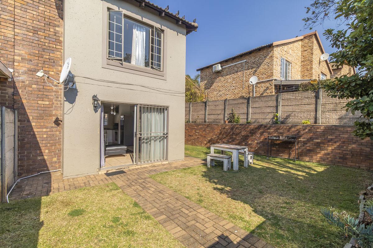 Rear exterior view of the townhouse featuring a private garden, brick paved pathway, and sliding door access to the interior living space.