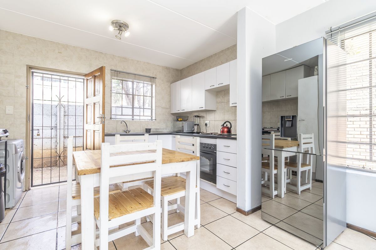 Functional kitchen featuring white cabinetry, tiled backsplash, built-in oven and hob, with direct access to an outdoor area through a security gate.
