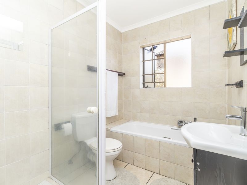A functional bathroom featuring a shower enclosure, bathtub, vanity basin, and toilet with neutral wall and floor tiling.
