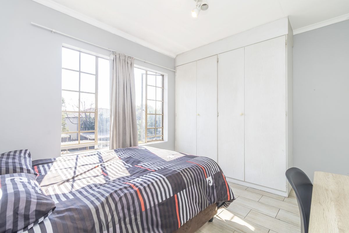 A bright bedroom featuring tiled flooring, large windows for natural light, and ample built-in cupboard storage space.