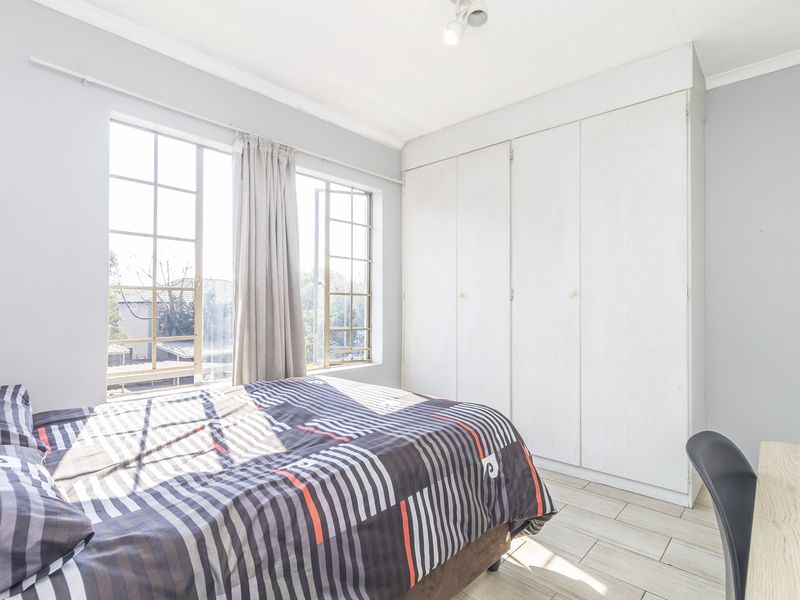 A bright bedroom featuring tiled flooring, large windows for natural light, and ample built-in cupboard storage space.