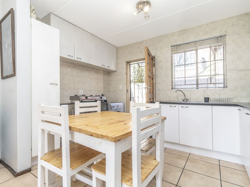 Functional kitchen featuring white cabinetry, tiled splashbacks, built-in oven and hob, with direct access to the exterior.
