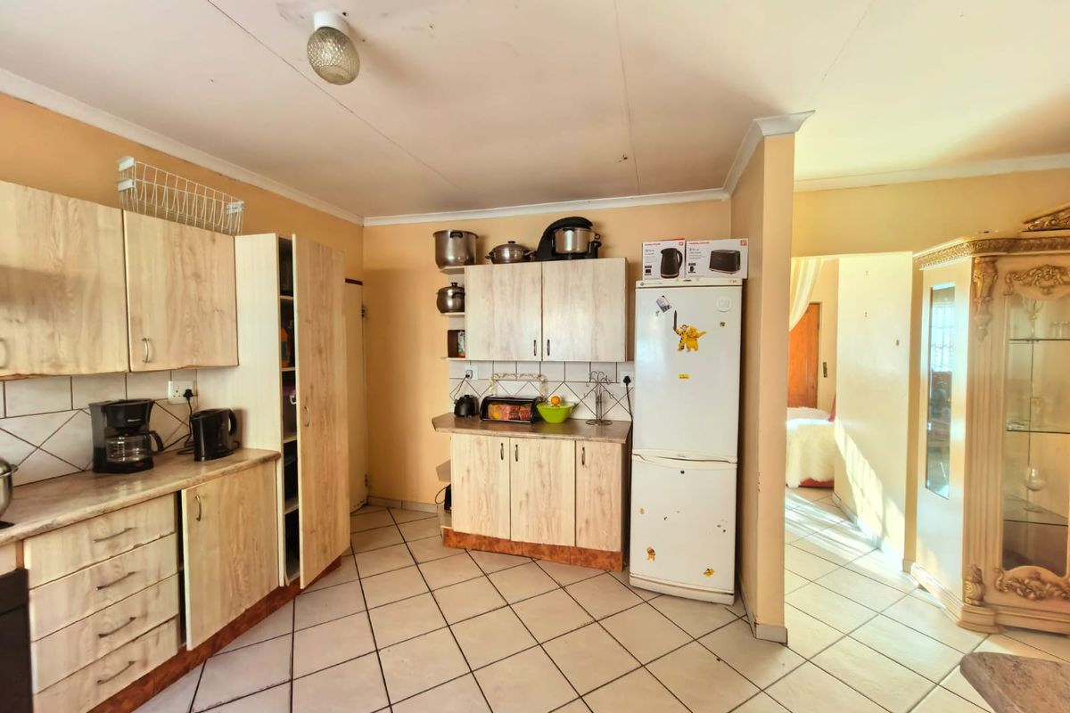 A functional kitchen featuring light wood-look laminate cabinetry, tiled flooring, and a tiled backsplash, offering a practical layout with potential for cosmetic updates.