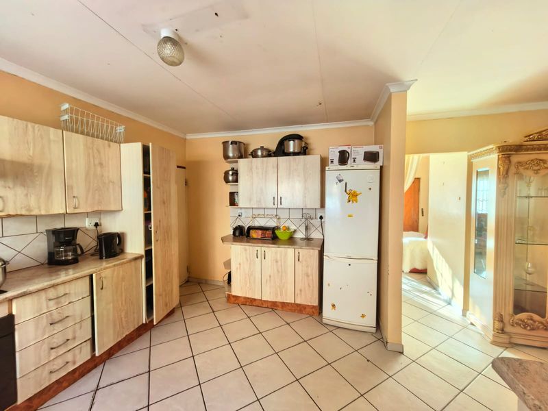 A functional kitchen featuring light wood-look laminate cabinetry, tiled flooring, and a tiled backsplash, offering a practical layout with potential for cosmetic updates.