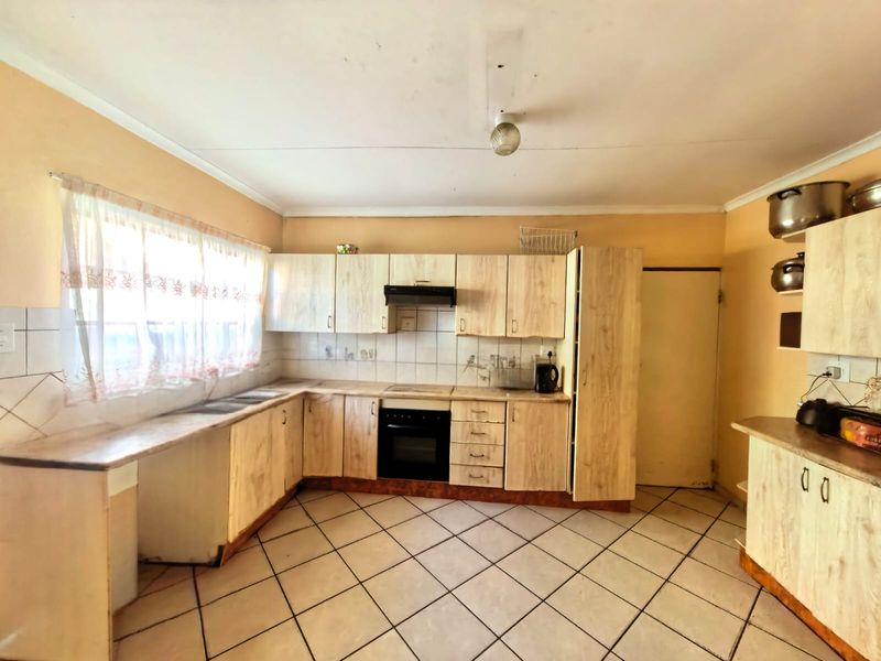 A functional kitchen featuring light wood-look cabinetry, built-in oven with extractor fan, tiled backsplash, and tiled flooring, offering potential for modern updates.