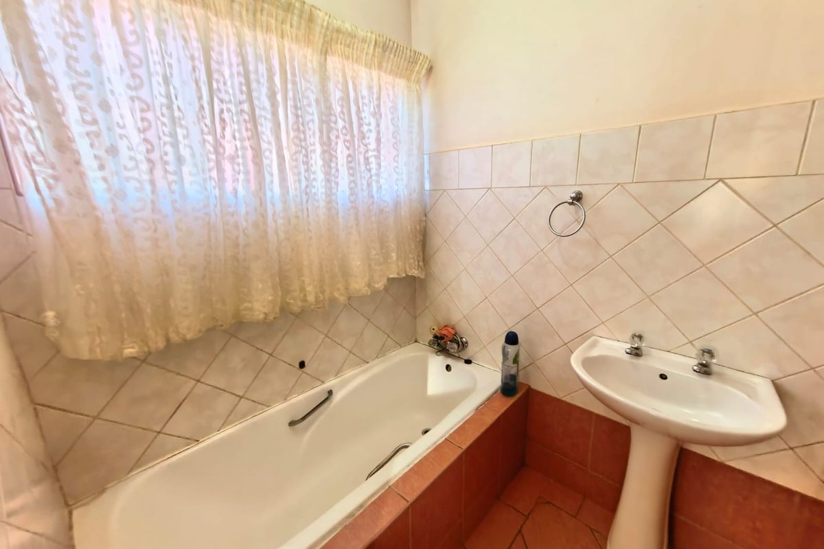 A functional bathroom featuring a built-in bathtub, pedestal washbasin, and tiled finishes, offering a dated aesthetic ready for modernization.