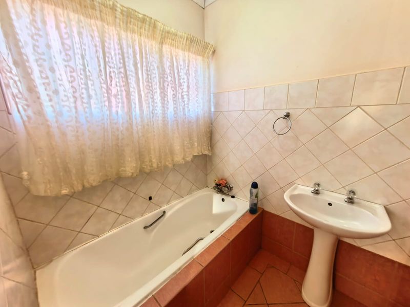 A functional bathroom featuring a built-in bathtub, pedestal washbasin, and tiled finishes, offering a dated aesthetic ready for modernization.