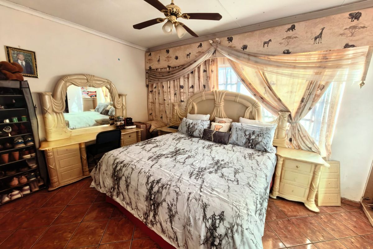 A bedroom featuring tiled flooring and a ceiling fan, currently furnished with a large bed and matching vanity unit.