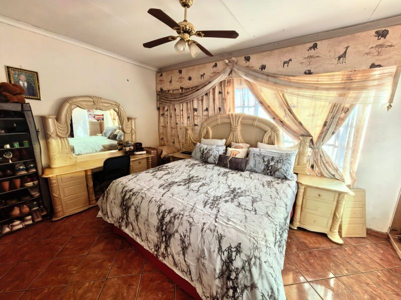 A bedroom featuring tiled flooring and a ceiling fan, currently furnished with a large bed and matching vanity unit.