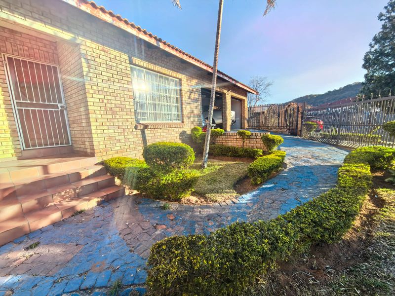 Front exterior view of a face brick house featuring a paved driveway, landscaped garden, and secure metal fencing.