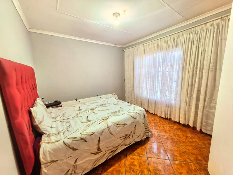 A bedroom featuring tiled flooring, ceiling cornice, and large window with curtain tracks. The room requires cosmetic updates to improve its overall condition.