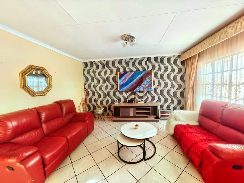 A well-lit living room featuring tiled flooring, a decorative patterned feature wall, and neutral wall finishes, providing a comfortable and functional living space.