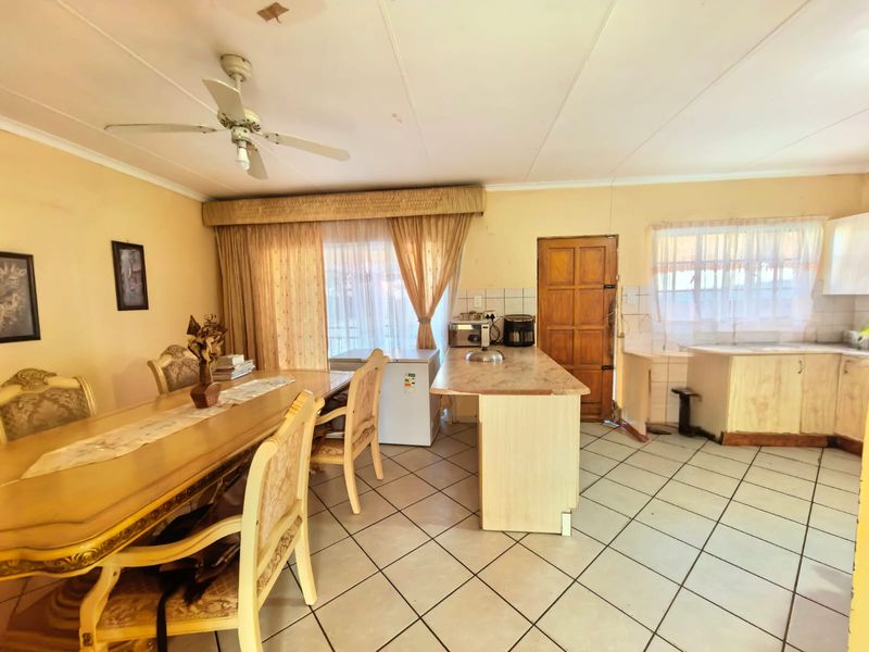 Open-plan dining and kitchen area featuring tiled flooring, dated cabinetry, and a ceiling fan, offering potential for a modern renovation.