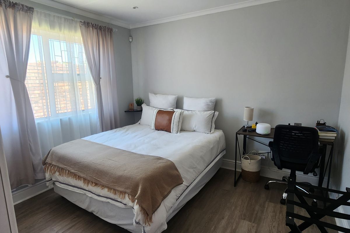 A well-maintained bedroom featuring laminate flooring, neutral wall finishes, and security bars on the window.