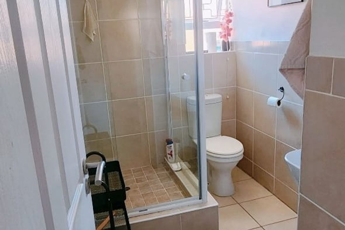 A functional bathroom featuring a glass-enclosed shower, a standard toilet, and neutral wall and floor tiling.