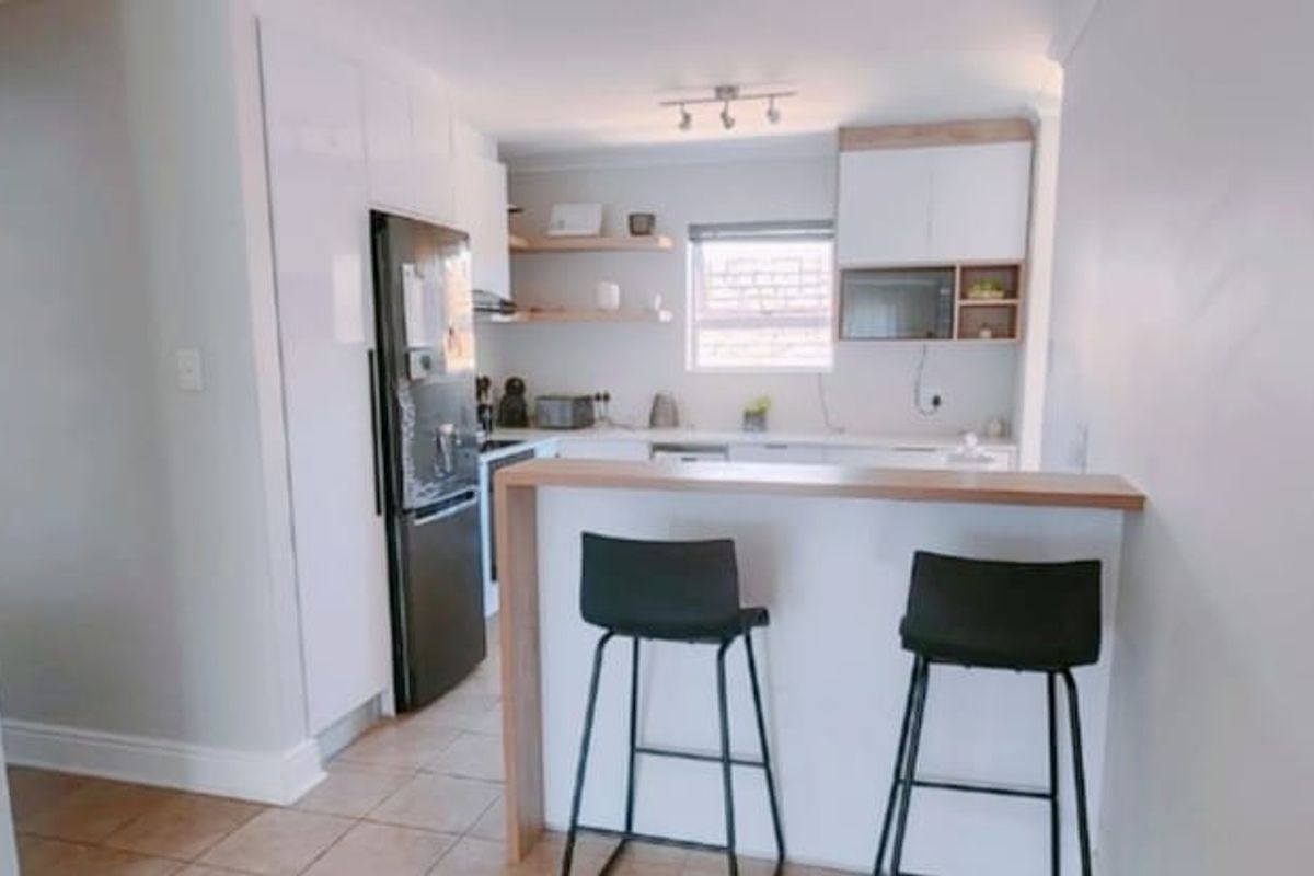 Modern kitchen featuring sleek white cabinetry, a functional breakfast bar, tiled flooring, and a unique glass block feature wall.