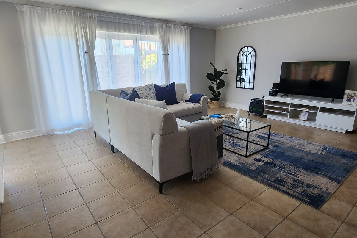 A well-maintained living room featuring neutral tiled flooring, cove cornicing, and a large sliding glass door providing natural light and access to the exterior.