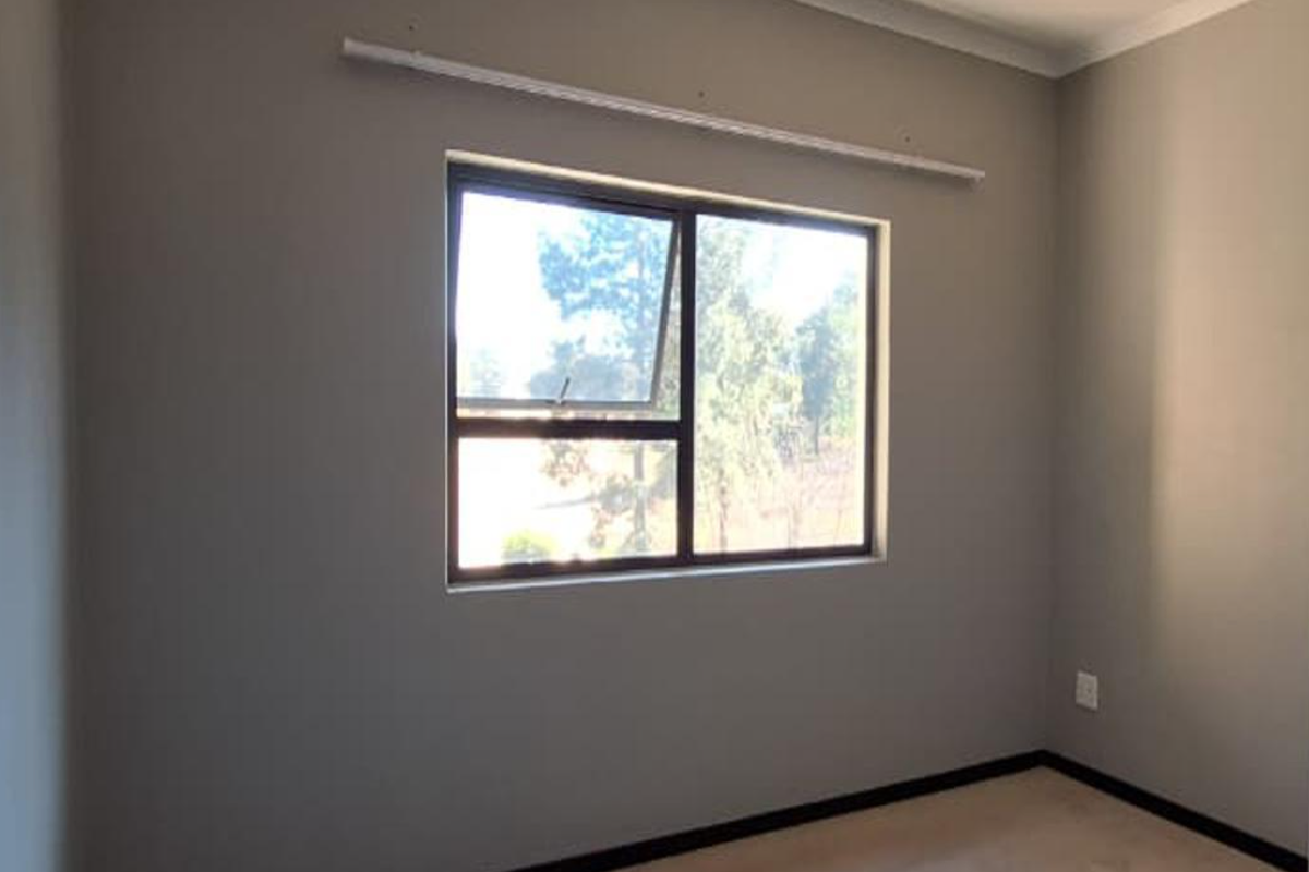 An empty bedroom featuring neutral grey walls, aluminium window frames, and dark skirting boards, ready for personalization.