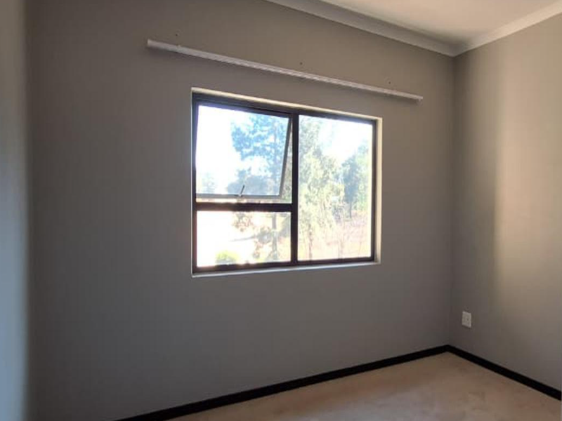 An empty bedroom featuring neutral grey walls, aluminium window frames, and dark skirting boards, ready for personalization.