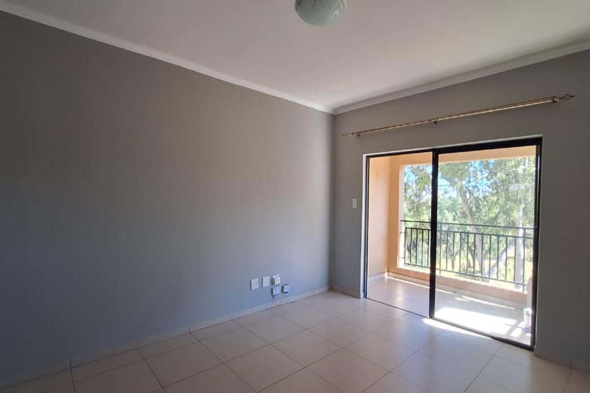 An empty living room featuring neutral grey walls, tiled flooring, and a sliding glass door providing access to a private balcony.
