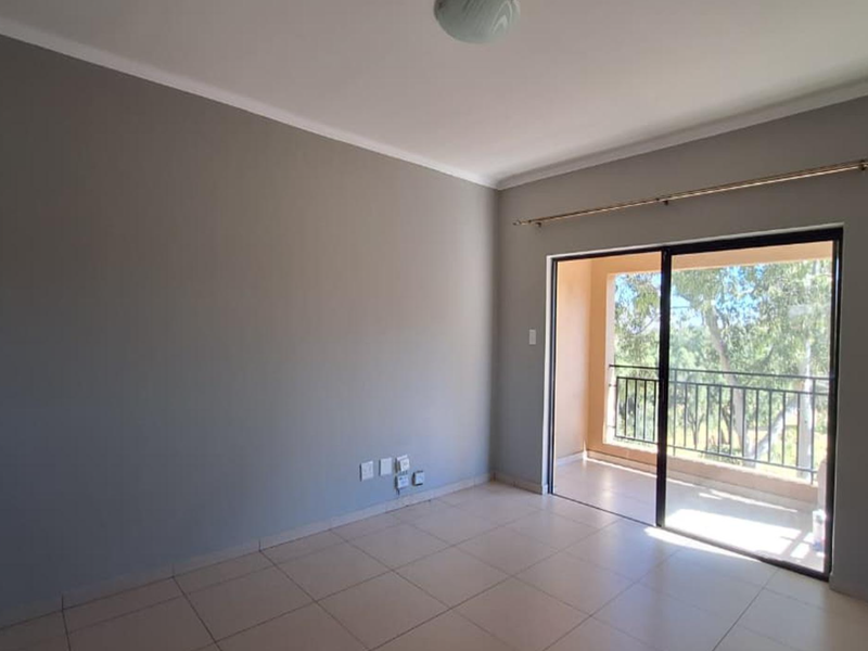 An empty living room featuring neutral grey walls, tiled flooring, and a sliding glass door providing access to a private balcony.