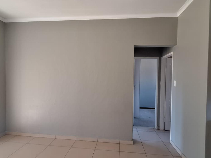 An open-plan living area featuring neutral grey walls, tiled flooring, and a sliding door leading to an outdoor space.