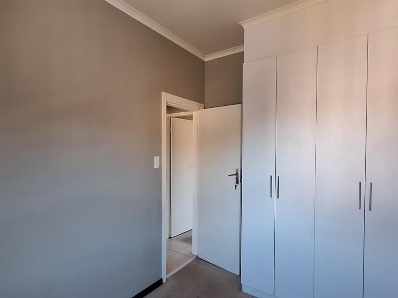 A clean, empty bedroom featuring neutral grey walls, white built-in cupboards, and coving detail, offering a blank canvas for personalization.
