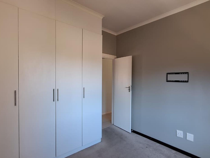 A clean, empty bedroom featuring neutral grey walls, built-in cupboards, and carpeted flooring, ready for personalization.