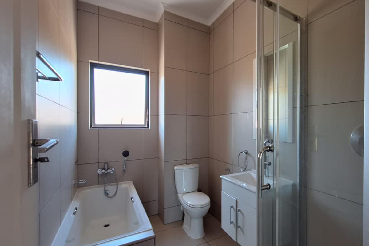 A modern, well-maintained bathroom featuring a built-in bathtub, separate shower enclosure, vanity cabinet, and neutral floor-to-ceiling wall tiles.