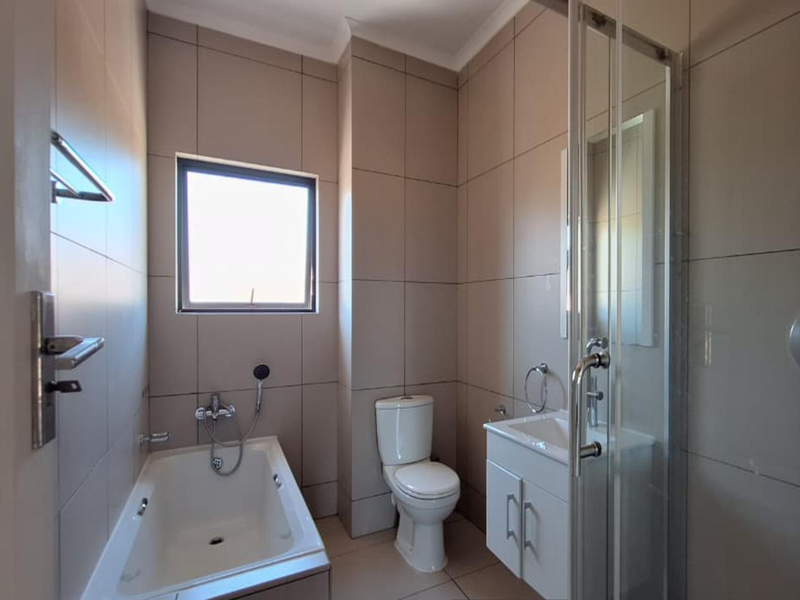 A modern, well-maintained bathroom featuring a built-in bathtub, separate shower enclosure, vanity cabinet, and neutral floor-to-ceiling wall tiles.