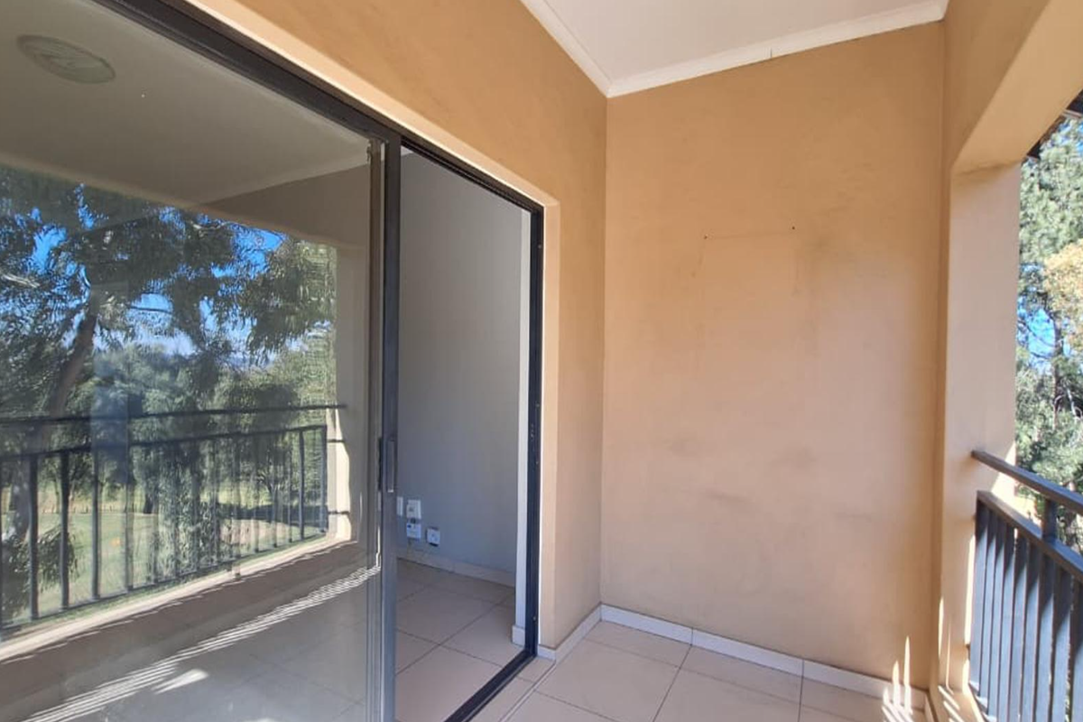 A covered balcony featuring tiled flooring, a metal balustrade, and a sliding glass door providing access to the interior living space.