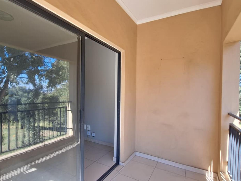 A covered balcony featuring tiled flooring, a metal balustrade, and a sliding glass door providing access to the interior living space.