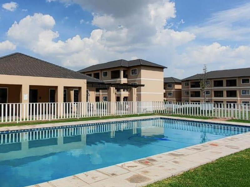 A well-maintained communal swimming pool area featuring paved surrounds and secure perimeter fencing within a modern apartment complex.