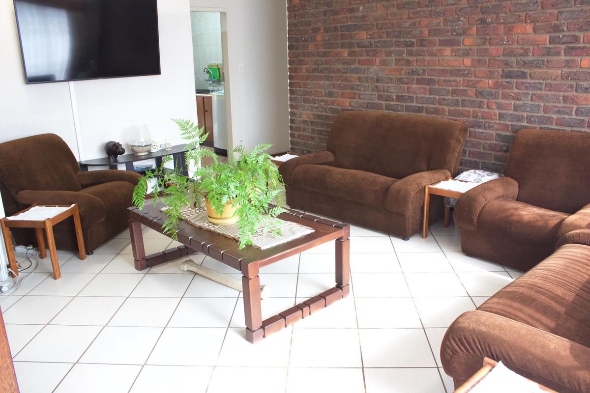 A living room featuring a prominent exposed brick feature wall and light-colored ceramic floor tiles, with an open doorway leading to an adjacent utility area.