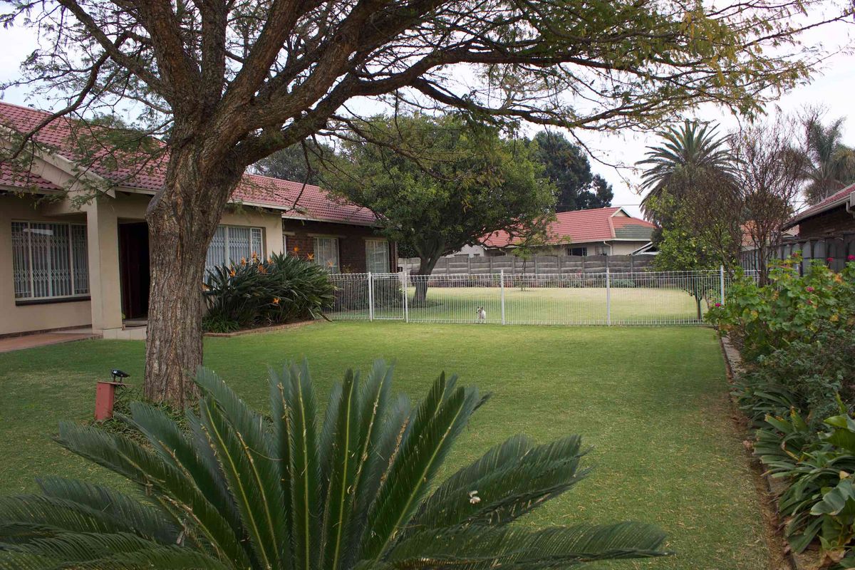A well-maintained rear garden featuring a spacious lawn, mature trees, and secure perimeter fencing with a view of the house exterior.