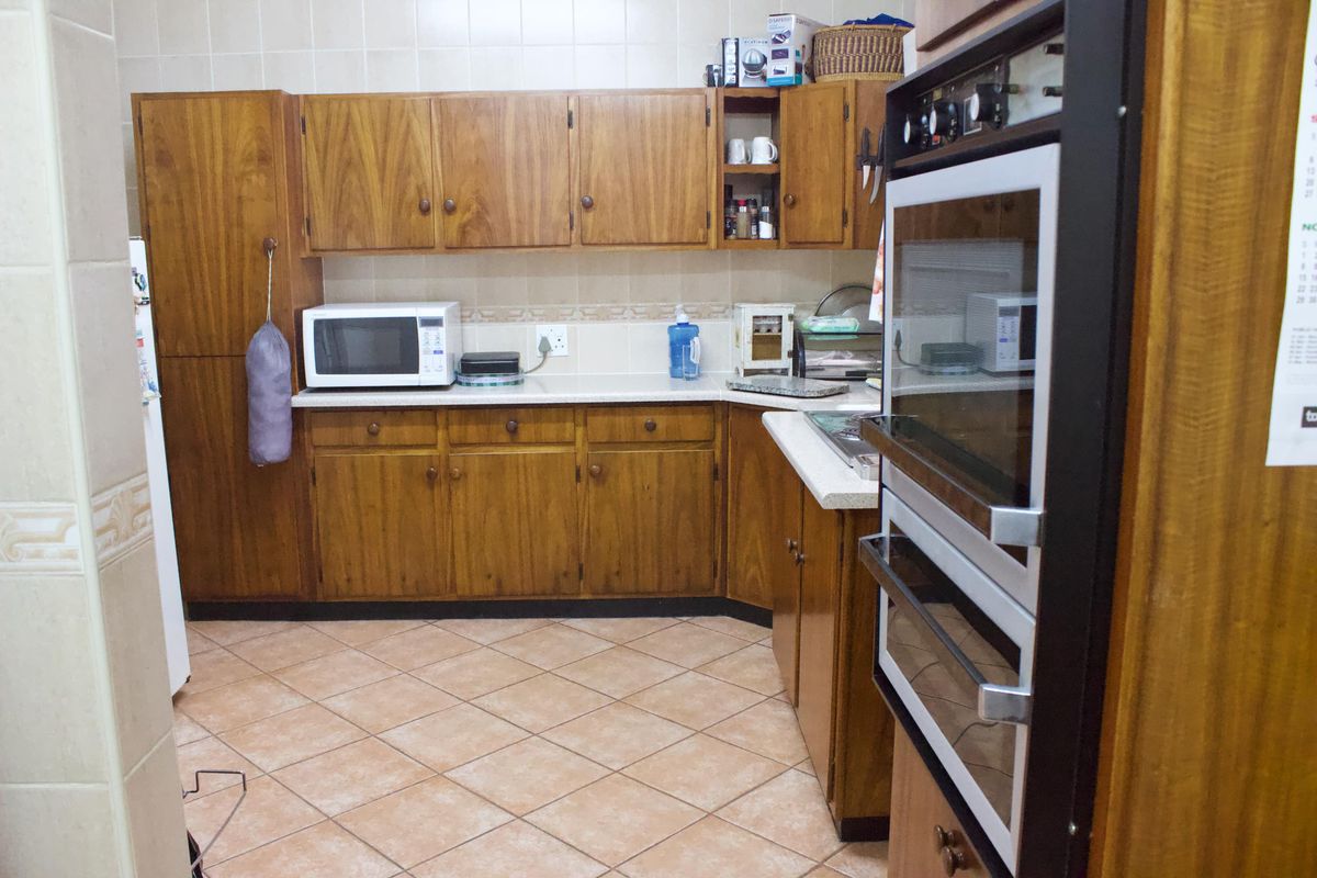 A functional kitchen featuring traditional wooden cabinetry, tiled flooring, and a built-in double oven, offering a classic layout with ample storage space.