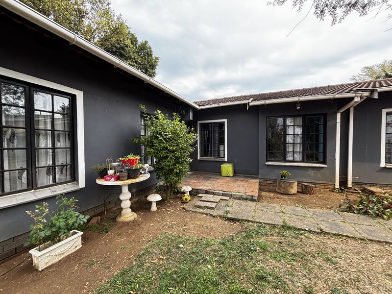 Rear exterior view of the house featuring a tiled patio area, concrete pathways, and dark-painted walls with multi-pane windows.