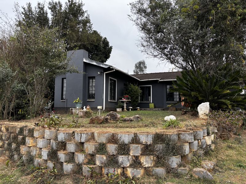 Rear view of a dark-painted house featuring a prominent chimney, tiled roof, and a tiered garden with a stone retaining wall.