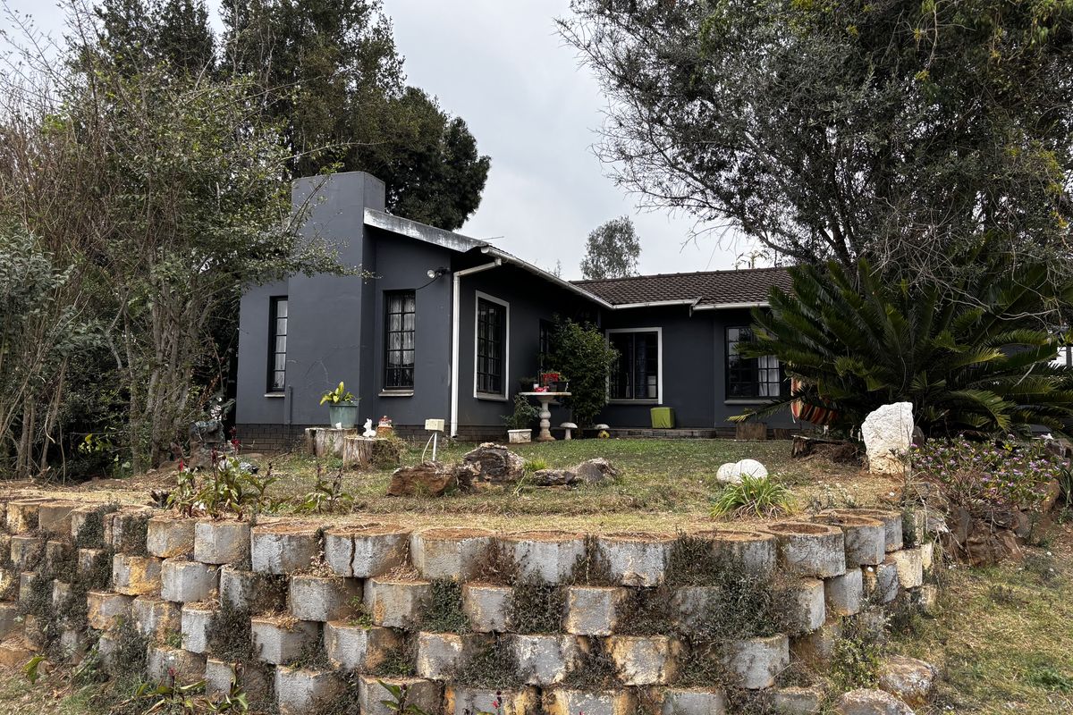 Rear view of a dark-painted house featuring a prominent chimney, tiled roof, and a tiered garden with a stone retaining wall.