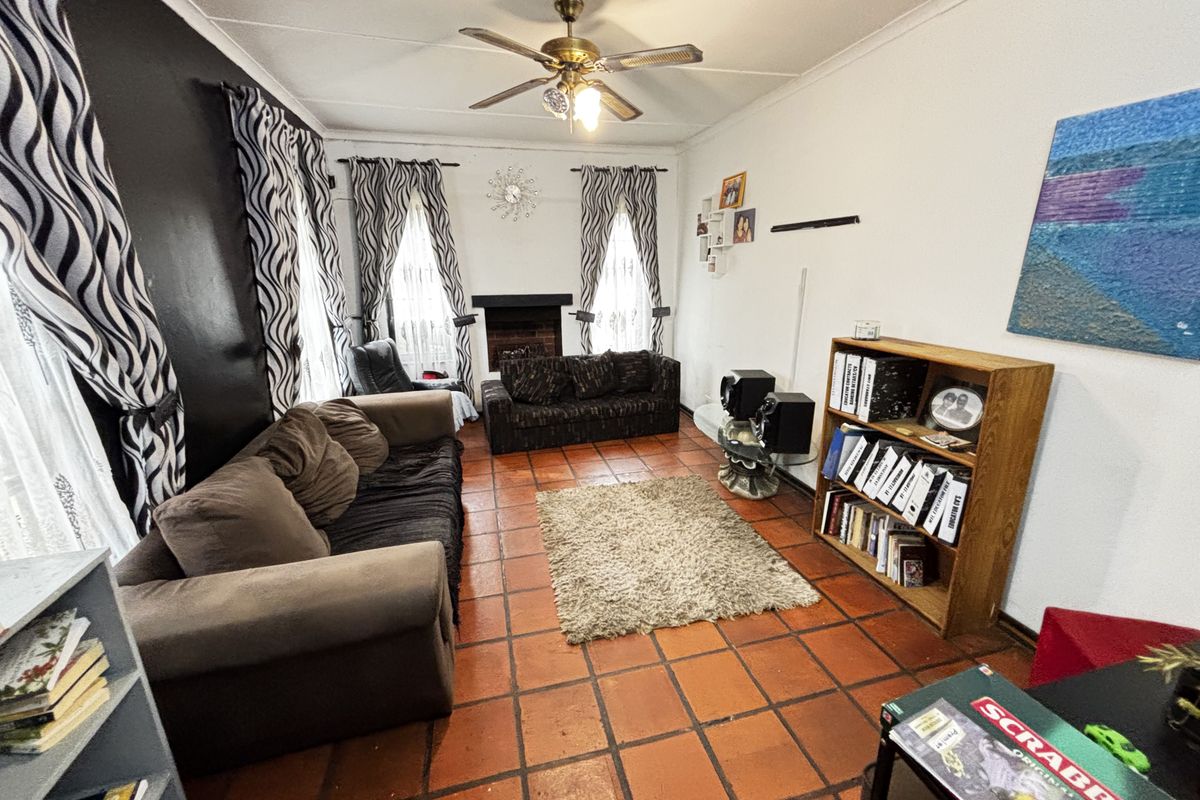 A living room featuring terracotta floor tiles, a central ceiling fan, and a brick fireplace as a focal point.
