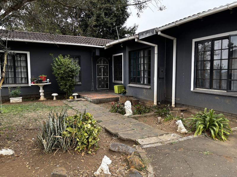 Front elevation of a single-story house featuring dark painted exterior walls, a tiled roof, and a paved walkway leading to the entrance.