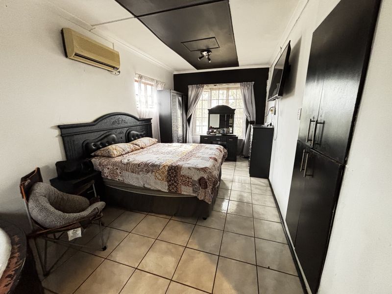 A bedroom featuring tiled flooring, built-in cupboards, and a recessed ceiling detail, providing a functional space with potential for cosmetic updates.