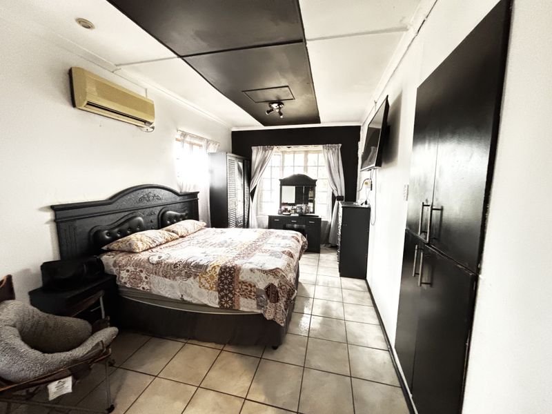 A bedroom featuring tiled flooring, built-in cupboards, and a split-system air conditioner, with a distinct black ceiling feature.