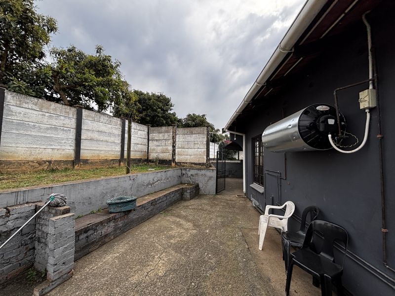 Rear exterior area featuring a concrete paved pathway, retaining wall, and boundary wall with an externally mounted geyser unit.