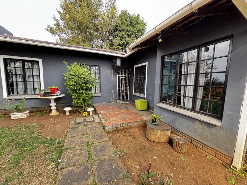 Rear exterior view of the house featuring a tiled patio area, stone pathway, and dark-painted exterior walls with security gate access.