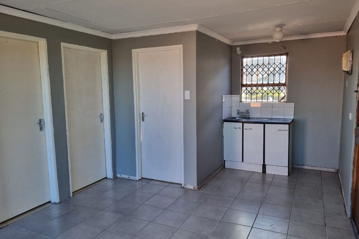 A compact, empty kitchen area featuring tiled flooring, basic base cabinetry with a sink, and a window fitted with a security gate.
