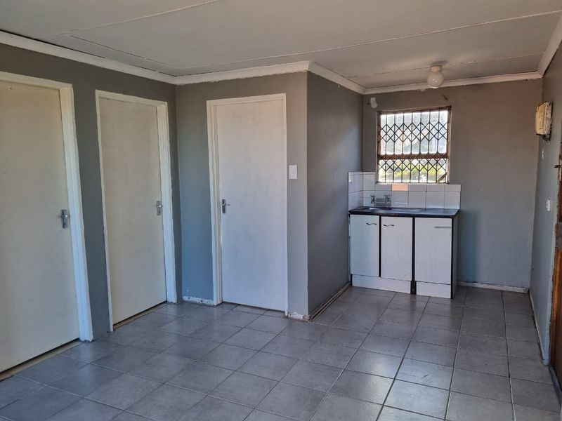 A compact, empty kitchen area featuring tiled flooring, basic base cabinetry with a sink, and a window fitted with a security gate.