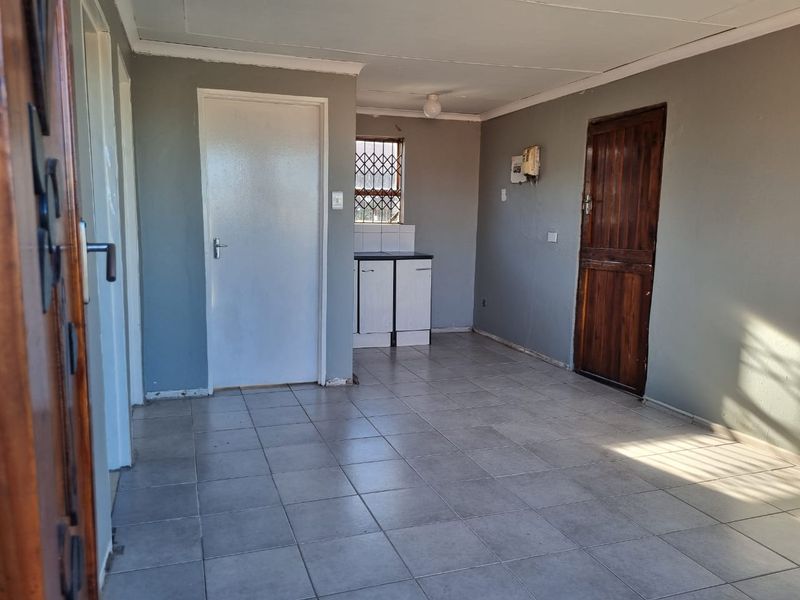An empty open-plan living area featuring tiled flooring, a small kitchenette corner, and direct access to multiple rooms.